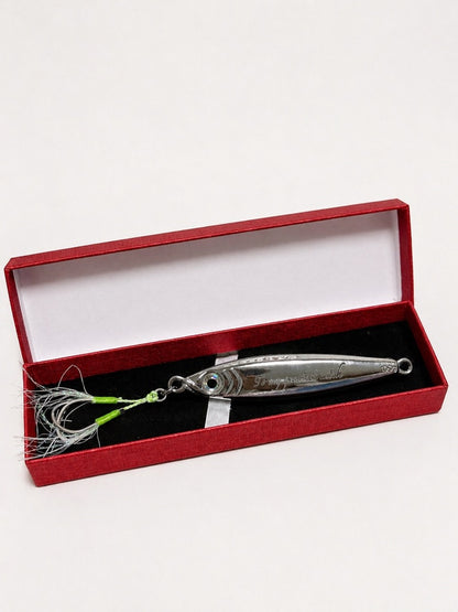 A silver metal fishing lure with a green and white skirt, presented inside an open red velvet box with a black insert on a white background.
