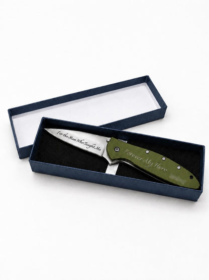 An engraved folding pocket knife with an olive green handle and a silver blade, presented inside an open dark blue gift box on a white background.