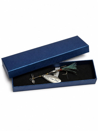 A silver spinnerbait fishing lure with a green and red feather tail, engraved with 'Love You Dad', presented in an open textured navy blue gift box with a black velvet interior.
