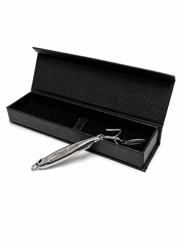 A silver metal hair clipper with engraved branding, displayed diagonally across an open black presentation box on a white background.