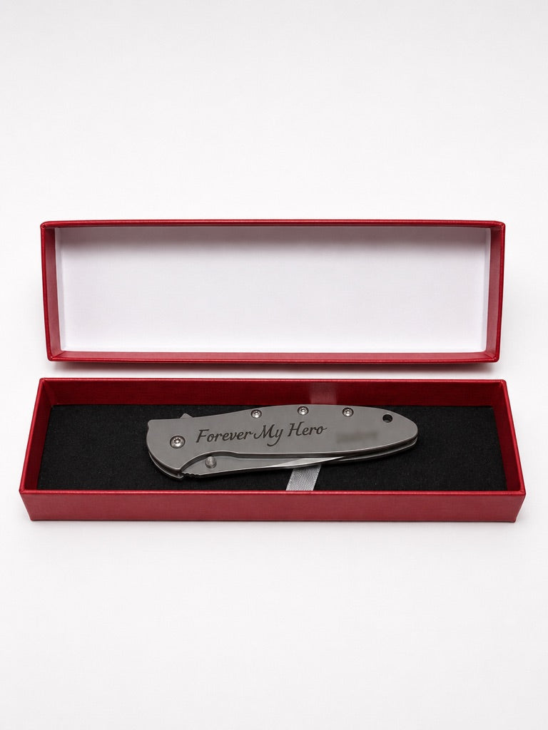 A folding pocket knife with 'Forever My Hero' engraved on the handle, presented inside an open red gift box with a black foam insert on a white background.