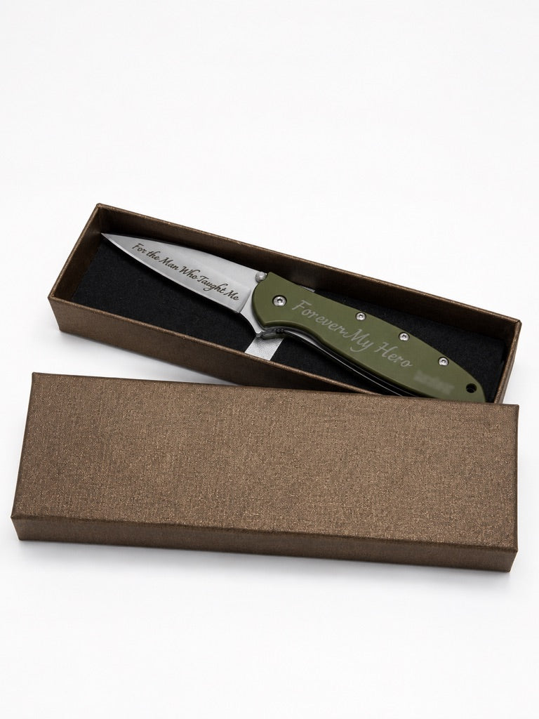An engraved folding pocket knife with an olive green handle and a silver blade, presented in an open textured brown gift box on a white background.