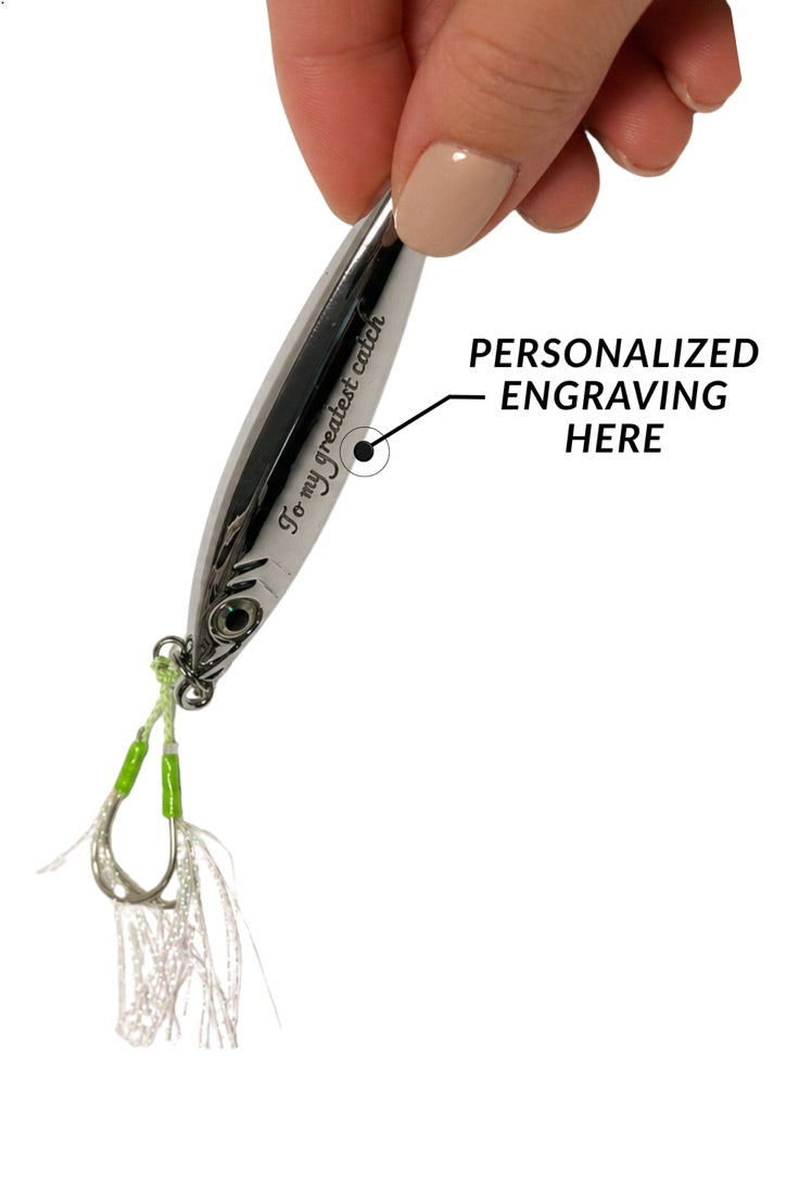 A close-up of a hand holding a silver metal fishing lure with a treble hook and white skirt. Black text on the lure reads '16 mi jettison depth' and there is an arrow pointing to the center with the words 'PERSONALIZED ENGRAVING HERE' to indicate where custom engraving is done.