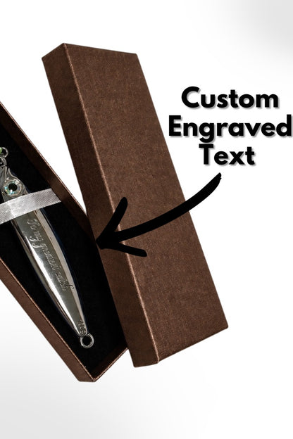 A silver dagger or letter opener displayed inside an open brown presentation box with a black insert, alongside a brown rectangular box lid and overlaid text reading 'Custom Engraved Text' with a black arrow pointing to the box.