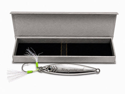 A silver metal fishing lure engraved with 'For my greatest catch' and '300 g', displayed in front of an open textured gray presentation box with a black interior.