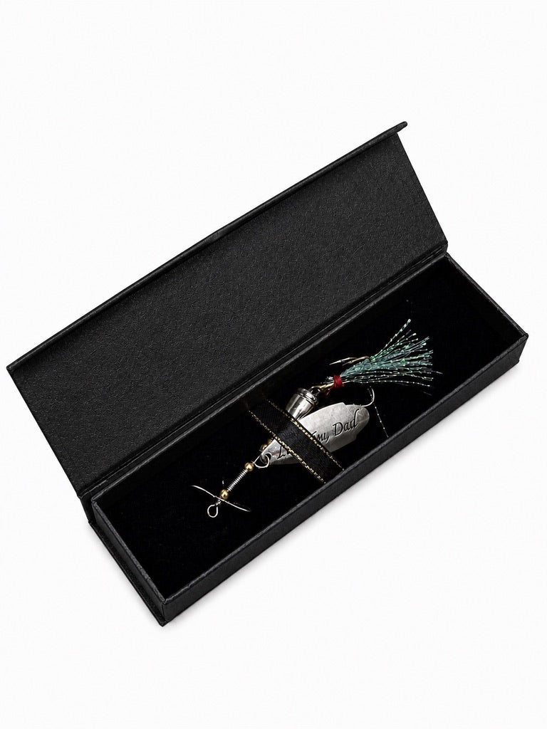 A silver metal fishing lure with a green and black skirt, presented inside an open black velvet gift box on a white background.