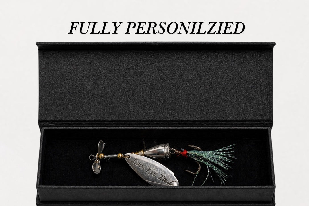A silver metal fishing lure with a green and red skirt is displayed inside an open black presentation box on a white background, with the text 'FULLY PERSONILZIED' above it.