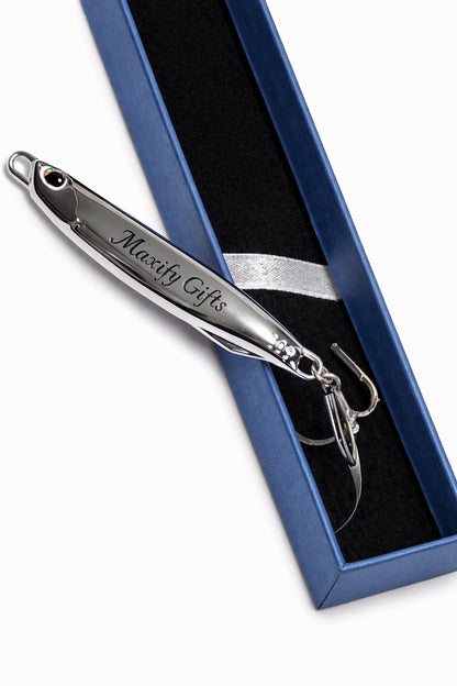 A silver metal novelty fishing lure engraved with 'Maxify Gifts' and displayed inside a blue presentation box with a black interior.