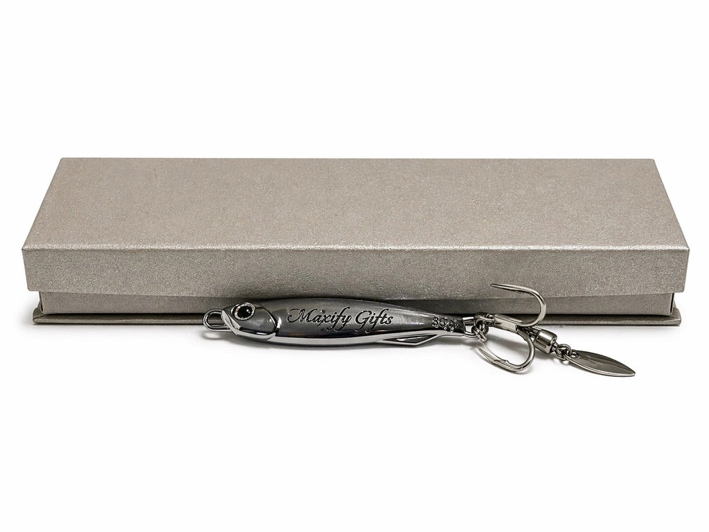 A silver metal fishing lure engraved with 'Moxify Gifts' resting in front of a textured gray presentation box on a white background.