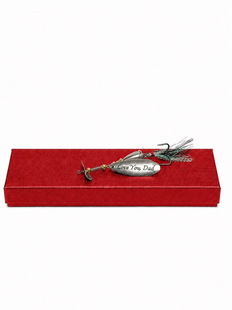 A silver metal fishing lure engraved with 'I Love You Dad' rests on a textured red gift box against a plain white background.