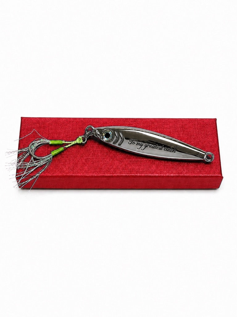 A silver metal fishing lure with a green and silver skirt, displayed on top of a red textured rectangular box against a white background.