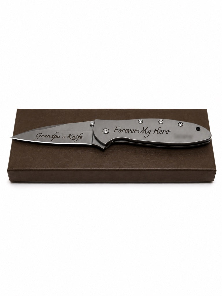 A personalized folding pocket knife with a satin finish, displayed on top of a brown presentation box. The blade is engraved with 'Grandpa's Knife' and the handle with 'Forever My Hero' in script.