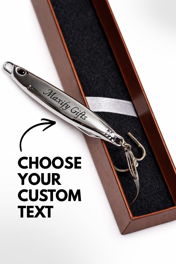 A silver metal fishing lure engraved with 'Maxify Gifts' resting inside an open brown presentation box with a black insert. Large text on the image reads 'CHOOSE YOUR CUSTOM TEXT' with an arrow pointing to the lure.