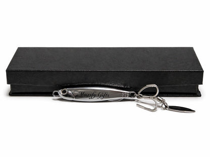 A silver metal novelty keychain shaped like a fishing lure, featuring an engraved nameplate that reads 'Majesty Gifts' and a small black key blade, displayed in front of a black presentation box on a white background.