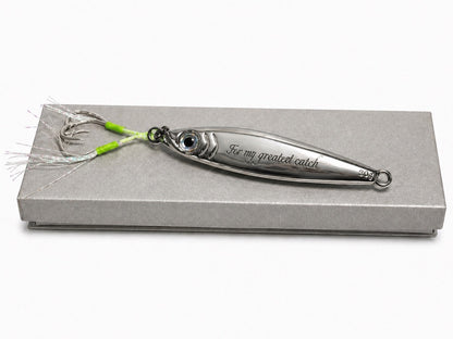A silver metal fishing lure with a fish-shaped body, engraved with 'For my greatest catch', displayed on a textured gray presentation box against a white background.