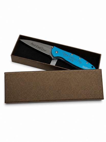 A folding pocket knife with a bright blue handle and a silver blade, presented in an open brown gift box on a white background. The blade is engraved with 'Best Duck Hunter' and the handle features 'Happy Hunting Day' and '2025'.