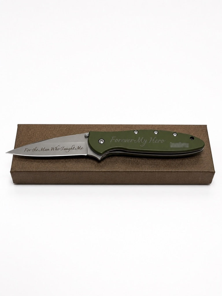 A custom engraved folding pocket knife with an olive green handle and a satin-finished steel blade, displayed on a brown presentation box against a white background.