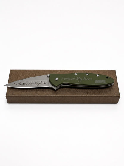 A custom engraved folding pocket knife with an olive green handle and a satin-finished steel blade, displayed on a brown presentation box against a white background.