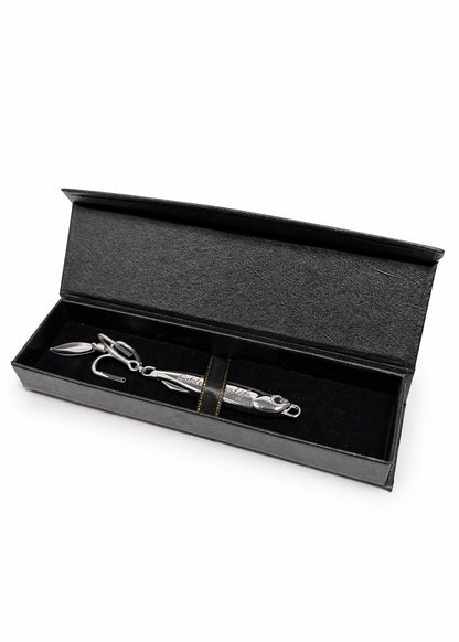 A silver metal fishing lure with a textured body and hook, presented inside an open black gift box with a black velvet interior on a white background.