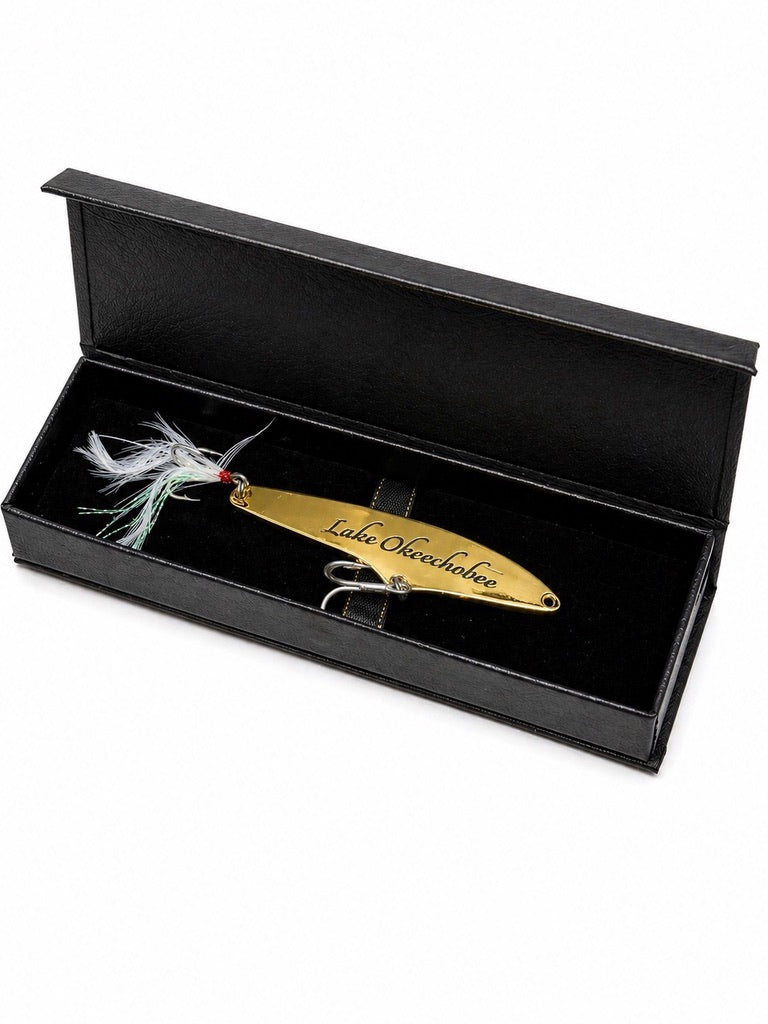 A gold metal fishing lure engraved with 'Lake Overlander' and displayed inside an open black presentation box with a black velvet insert.