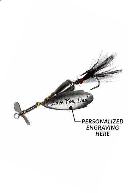 A silver metal fishing lure with a black feather tail and a propeller, shown on a white background with a callout indicating personalized engraving on the side.