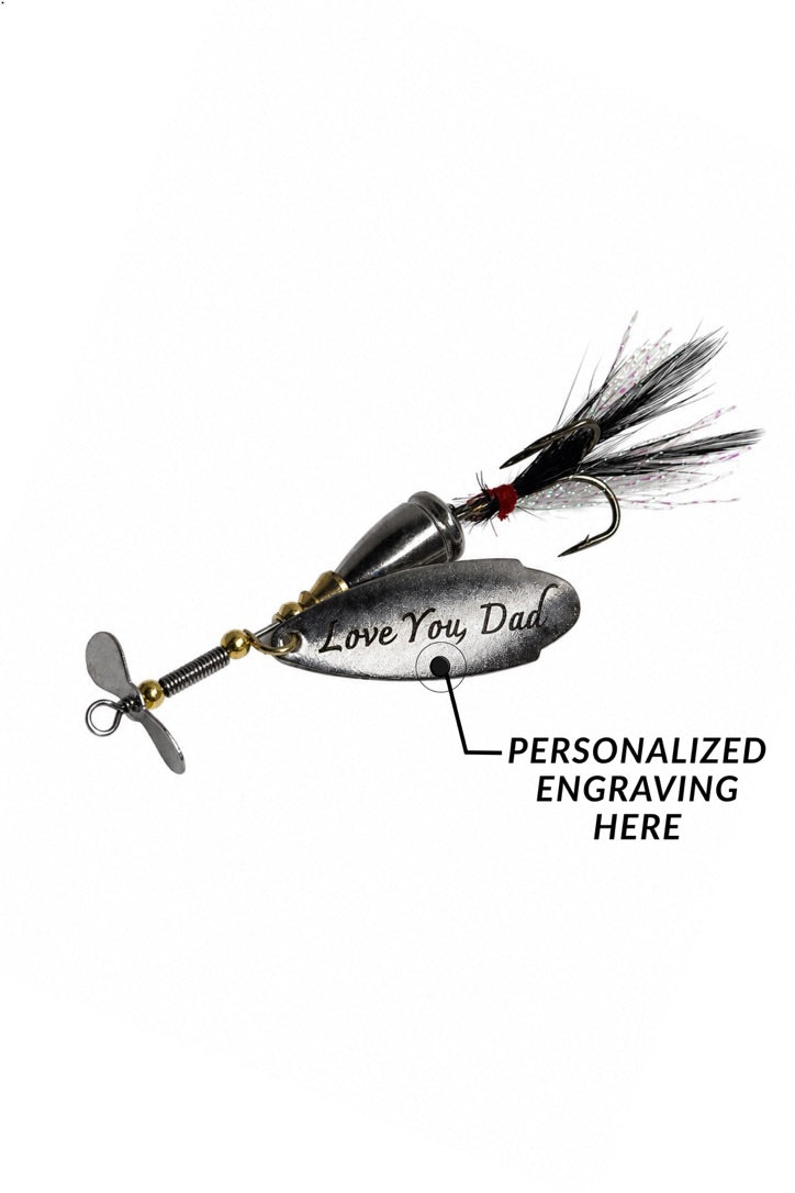 A silver metal fishing lure with a black feather tail and a propeller, shown on a white background with a callout indicating personalized engraving on the side.