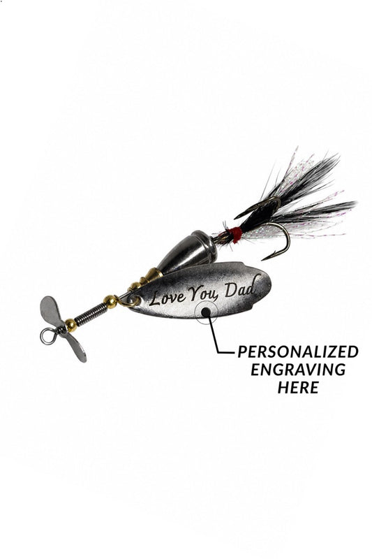 A silver metal fishing lure with a black feather tail and a propeller, shown on a white background with a callout indicating personalized engraving on the side.