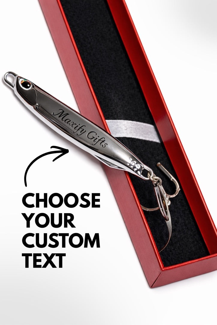 A silver metal fishing lure engraved with 'Maxity Gifts' resting inside an open red presentation box with a black insert. Large text on the left reads 'CHOOSE YOUR CUSTOM TEXT' with an arrow pointing to the lure.
