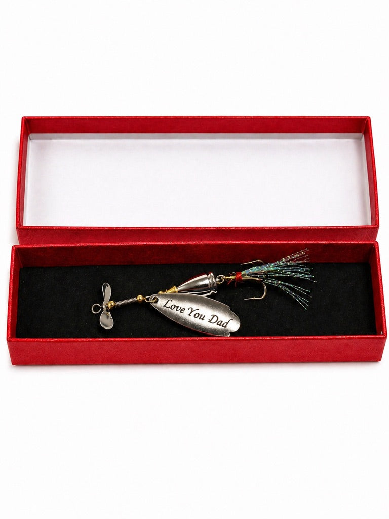 A silver metal spinnerbait fishing lure engraved with 'Love You Dad' is presented inside an open red velvet gift box with a black velvet insert on a white background.