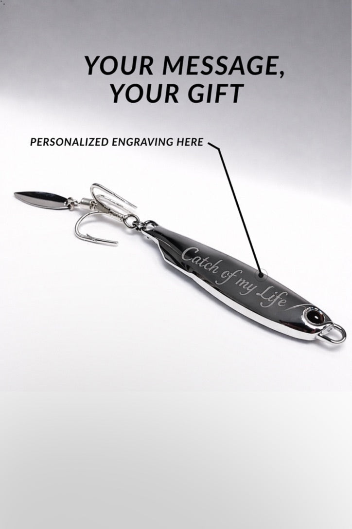 A silver metal fishing lure with a hook and blade, shown on a light gray background with promotional text reading 'YOUR MESSAGE, YOUR GIFT' and 'PERSONALIZED ENGRAVING HERE.' The lure has engraved script text on its body.