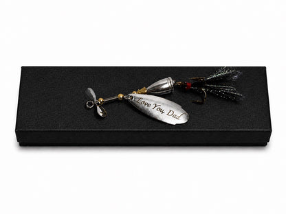 A silver metal fishing lure engraved with 'I Love You Dad' resting on a black presentation box against a white background.