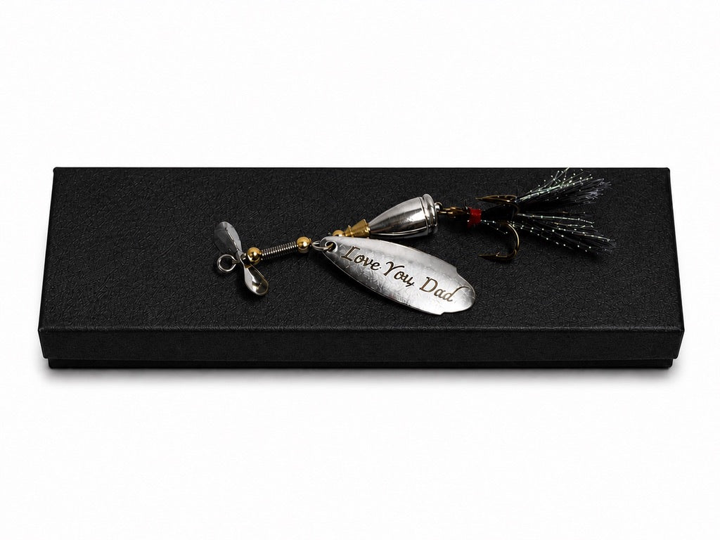 A silver metal fishing lure engraved with 'I Love You Dad' resting on a black presentation box against a white background.