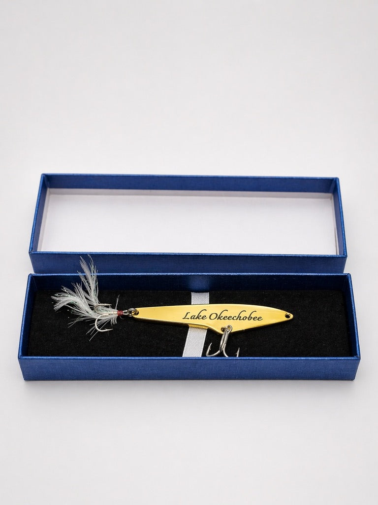 A gold metal fishing lure engraved with 'Lake Opechtopa' and presented in an open blue gift box with a black velvet insert.